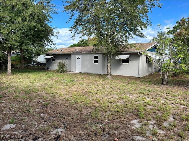 back of property with a lawn and stucco siding