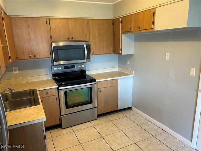 kitchen featuring baseboards, appliances with stainless steel finishes, light countertops, and a sink