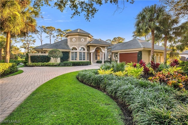 mediterranean / spanish-style house with a tiled roof, decorative driveway, an attached garage, and stucco siding