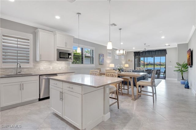 kitchen with stainless steel appliances, hanging light fixtures, white cabinets, a sink, and a kitchen island