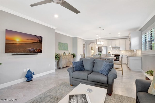 living area with ornamental molding, arched walkways, ceiling fan, and baseboards