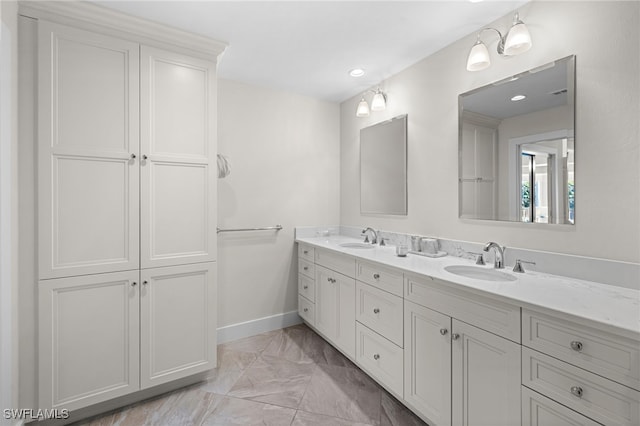 full bath featuring marble finish floor, double vanity, a sink, and baseboards