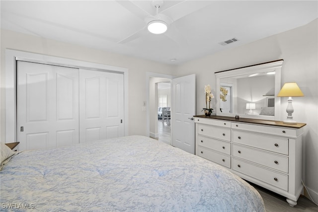 bedroom with baseboards, visible vents, ceiling fan, wood finished floors, and a closet