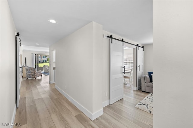 corridor featuring a barn door, recessed lighting, light wood-style flooring, and baseboards