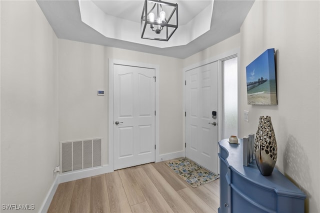 foyer entrance featuring a tray ceiling, light wood-type flooring, visible vents, and baseboards