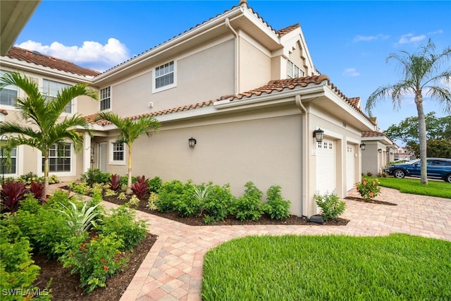 view of side of home with a tile roof, an attached garage, and stucco siding