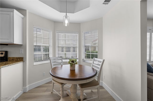 dining room featuring a tray ceiling, light wood-type flooring, visible vents, and baseboards