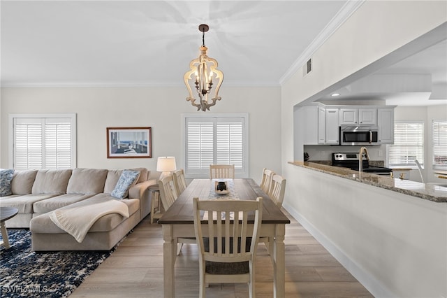 dining room with a chandelier, light wood-type flooring, visible vents, and crown molding