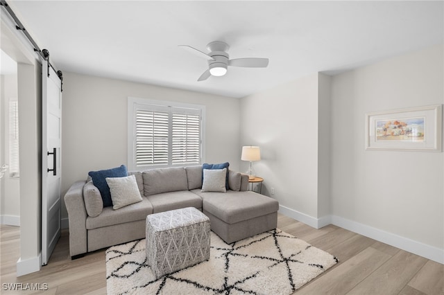 living area with ceiling fan, a barn door, baseboards, and light wood-style floors