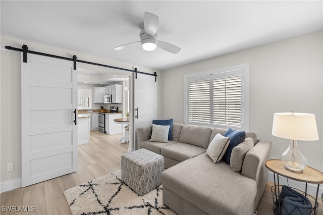 living room with a barn door, light wood-type flooring, a ceiling fan, and baseboards