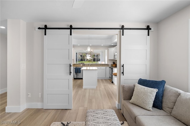 living area with light wood finished floors, a barn door, recessed lighting, and baseboards