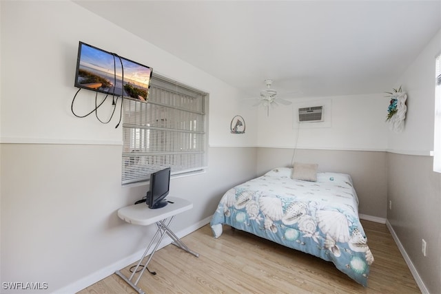 bedroom with a wall unit AC, wood finished floors, a ceiling fan, and baseboards