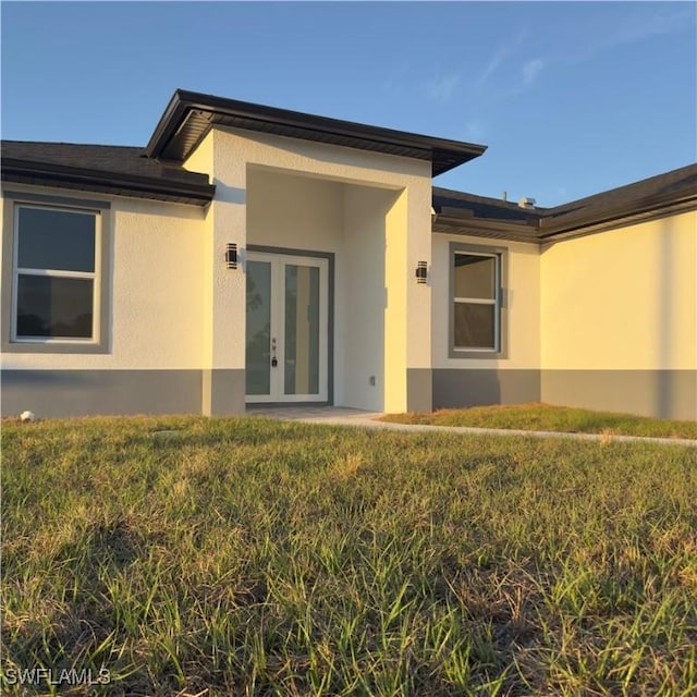 property entrance with a lawn, french doors, and stucco siding