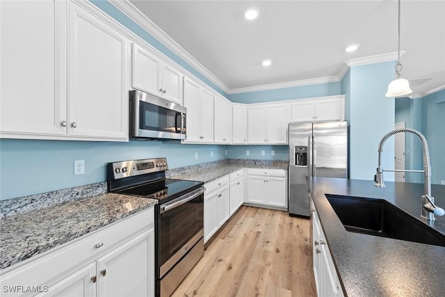 kitchen with stainless steel appliances, a sink, white cabinetry, dark stone countertops, and crown molding