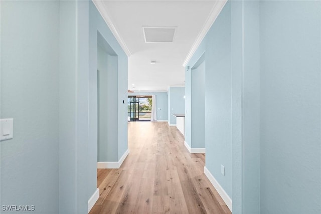 hallway with light wood-type flooring, visible vents, crown molding, and baseboards