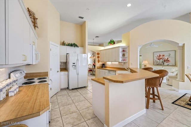 kitchen featuring arched walkways, white appliances, light tile patterned flooring, and a kitchen bar