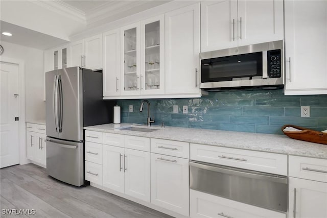 kitchen featuring crown molding, decorative backsplash, appliances with stainless steel finishes, white cabinets, and a sink