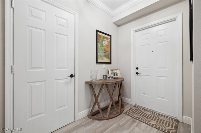 entryway with light wood-style flooring, ornamental molding, and baseboards