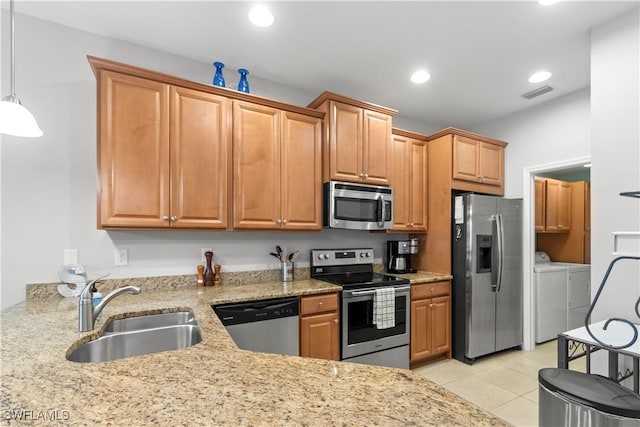 kitchen featuring light stone counters, independent washer and dryer, stainless steel appliances, a sink, and light tile patterned flooring