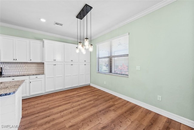 unfurnished dining area with light wood finished floors, baseboards, visible vents, and crown molding