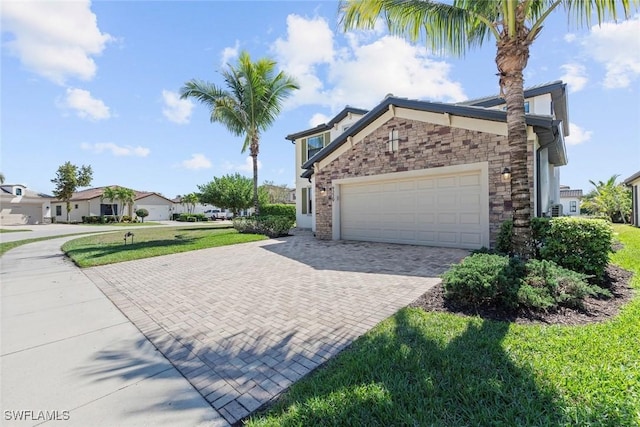 view of side of home featuring a garage, stone siding, a lawn, and decorative driveway