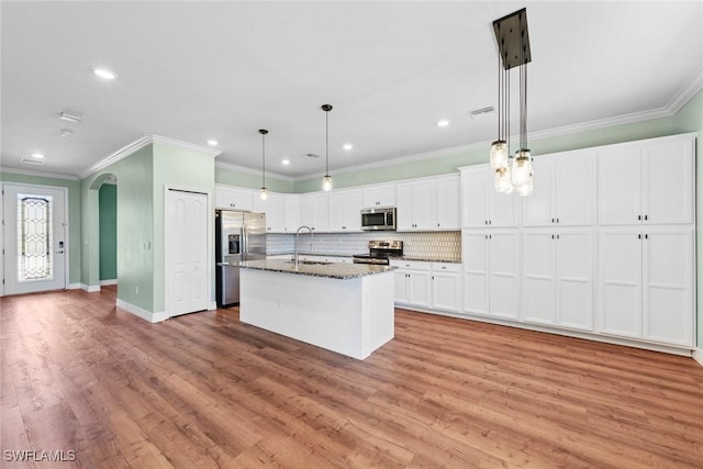 kitchen featuring arched walkways, stainless steel appliances, a sink, white cabinetry, and a center island with sink