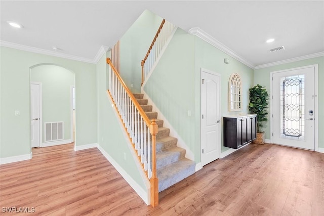 foyer with light wood finished floors, visible vents, arched walkways, and crown molding