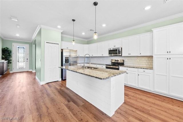 kitchen featuring a center island with sink, appliances with stainless steel finishes, a sink, light stone countertops, and backsplash