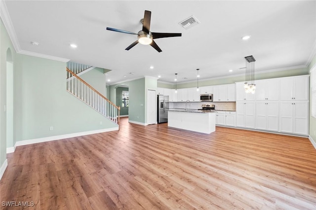 unfurnished living room featuring arched walkways, visible vents, light wood-style floors, stairway, and crown molding