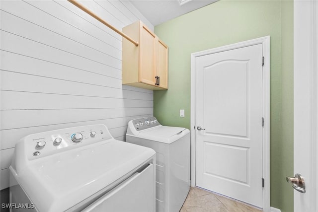 washroom featuring wood walls, light tile patterned flooring, washing machine and dryer, and cabinet space