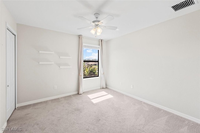 carpeted spare room with baseboards, visible vents, and a ceiling fan