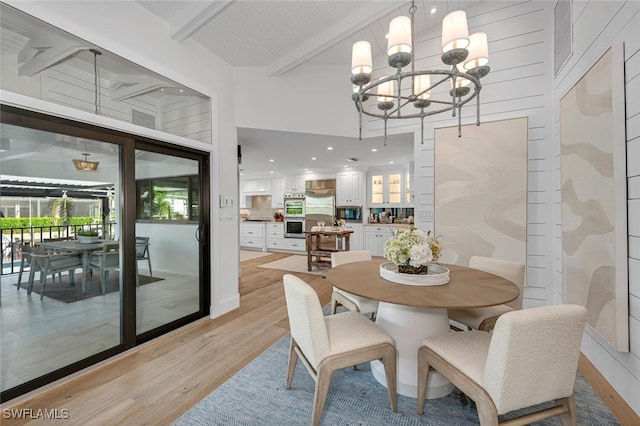 dining room with a towering ceiling, light wood-style flooring, a chandelier, and beam ceiling