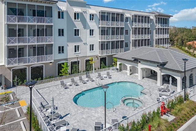 community pool with a patio area, fence, and a hot tub