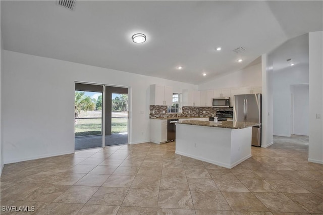 kitchen with white cabinets, decorative backsplash, a kitchen island, dark stone countertops, and stainless steel appliances