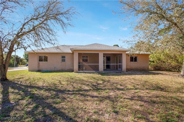 back of property with a yard, a sunroom, and stucco siding