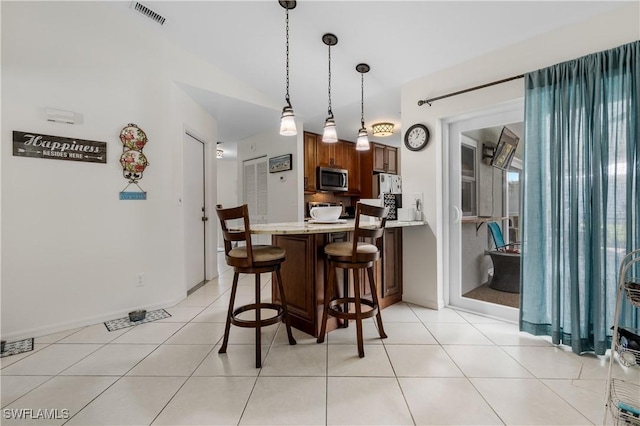 kitchen featuring visible vents, stainless steel microwave, a breakfast bar, a peninsula, and light countertops