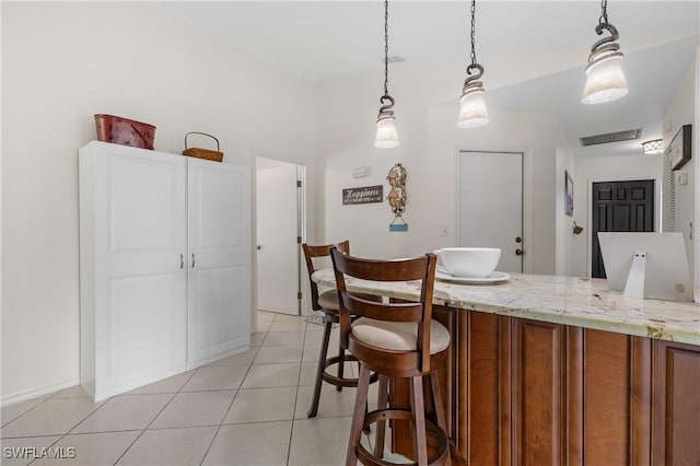 kitchen featuring light tile patterned floors, brown cabinetry, light stone counters, a breakfast bar, and pendant lighting