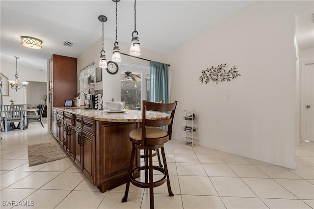 kitchen with light tile patterned floors, light stone counters, visible vents, a kitchen bar, and pendant lighting