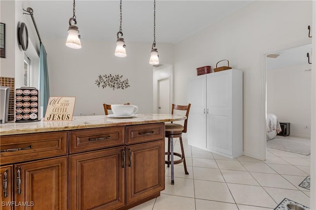 kitchen with light tile patterned floors, brown cabinets, light stone countertops, a kitchen bar, and pendant lighting