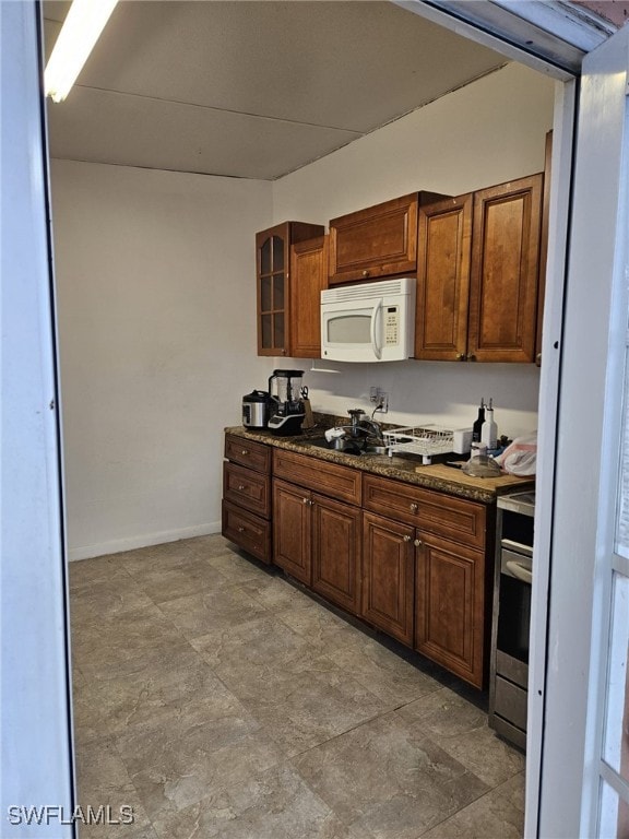 kitchen featuring white microwave, baseboards, stainless steel electric stove, dark stone countertops, and glass insert cabinets