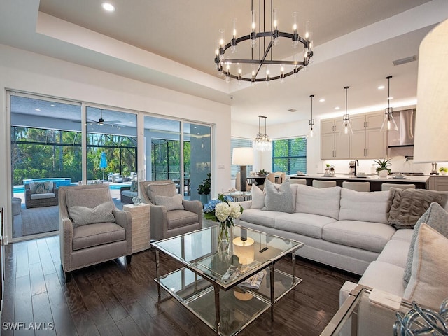 living room with a tray ceiling, dark wood finished floors, recessed lighting, visible vents, and a sunroom