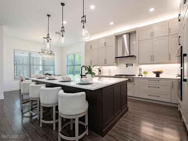 kitchen featuring stainless steel gas cooktop, dark wood-style flooring, light countertops, wall chimney exhaust hood, and a center island with sink