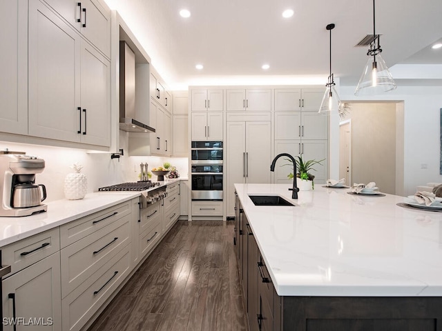 kitchen with visible vents, appliances with stainless steel finishes, dark wood-type flooring, a sink, and wall chimney range hood