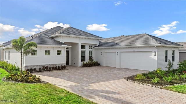 view of front facade featuring stucco siding, driveway, stone siding, an attached garage, and a tiled roof