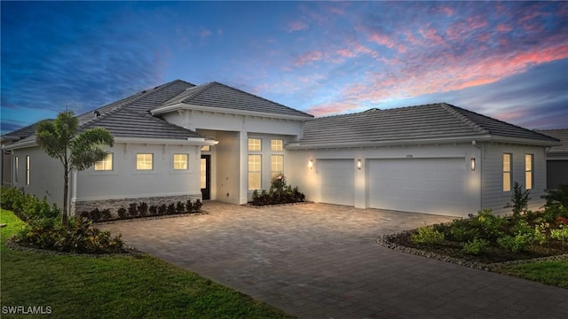 view of front facade with stucco siding, a garage, stone siding, a tiled roof, and decorative driveway