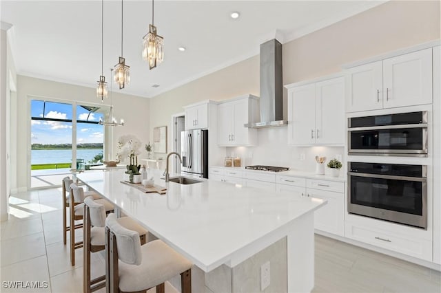 kitchen featuring a large island, a sink, stainless steel appliances, wall chimney exhaust hood, and a chandelier