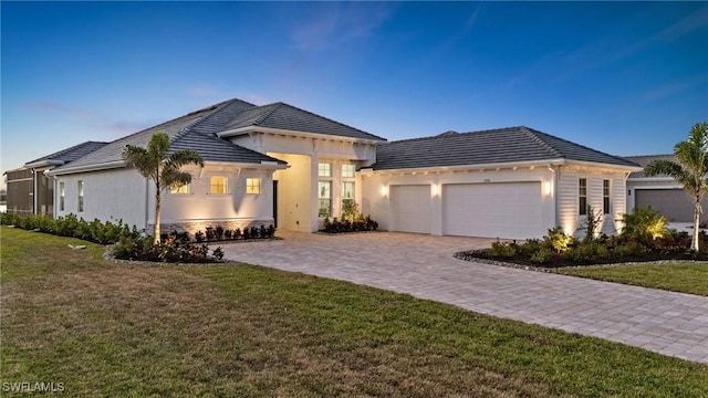 ranch-style home with a tile roof, a front yard, stucco siding, decorative driveway, and an attached garage