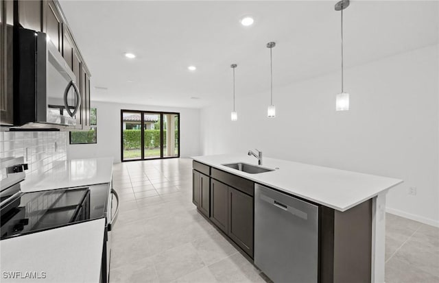 kitchen with stainless steel appliances, light countertops, hanging light fixtures, a sink, and an island with sink