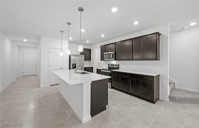 kitchen with pendant lighting, stainless steel appliances, light countertops, a sink, and an island with sink