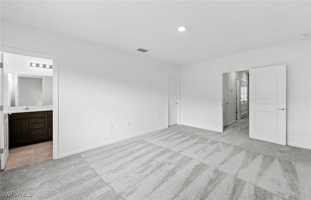 unfurnished bedroom with light colored carpet, visible vents, a sink, ensuite bath, and baseboards